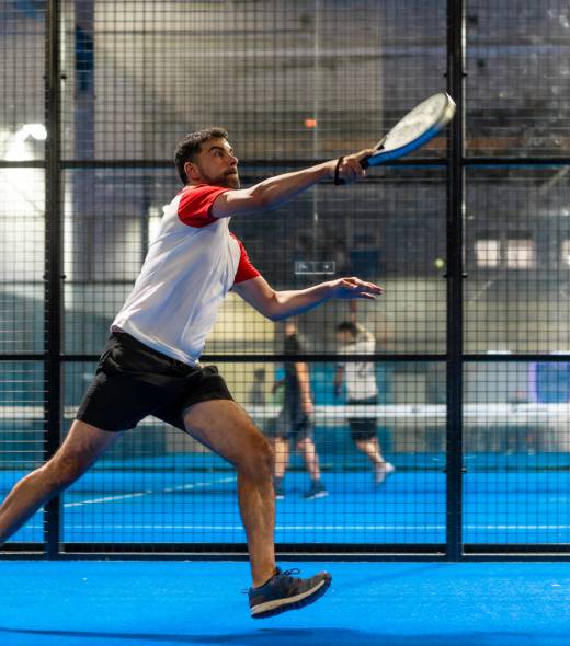 Full length photo of a mature sportive man trying to reach the ball while playing paddle tennis in an indoor court