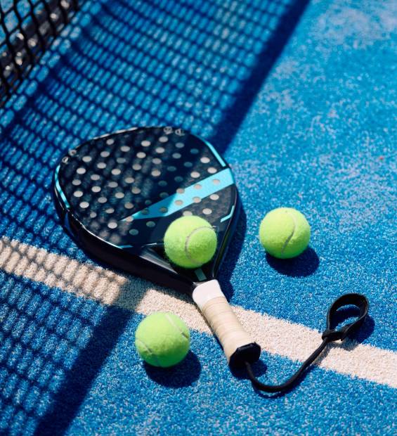 Paddle tennis racket and balls on blue outdoor court. Copy space.