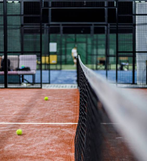Players engage in padel practice on an indoor court with balls scattered around.