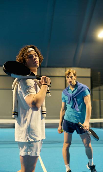 Two young sportsmen showcase their padel skills indoors under bright lights.